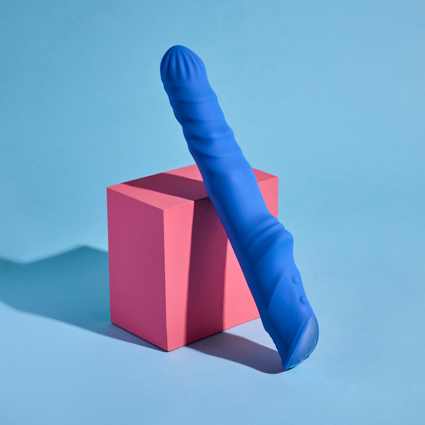 Blue silicone vibrator on a pink cube against a blue background