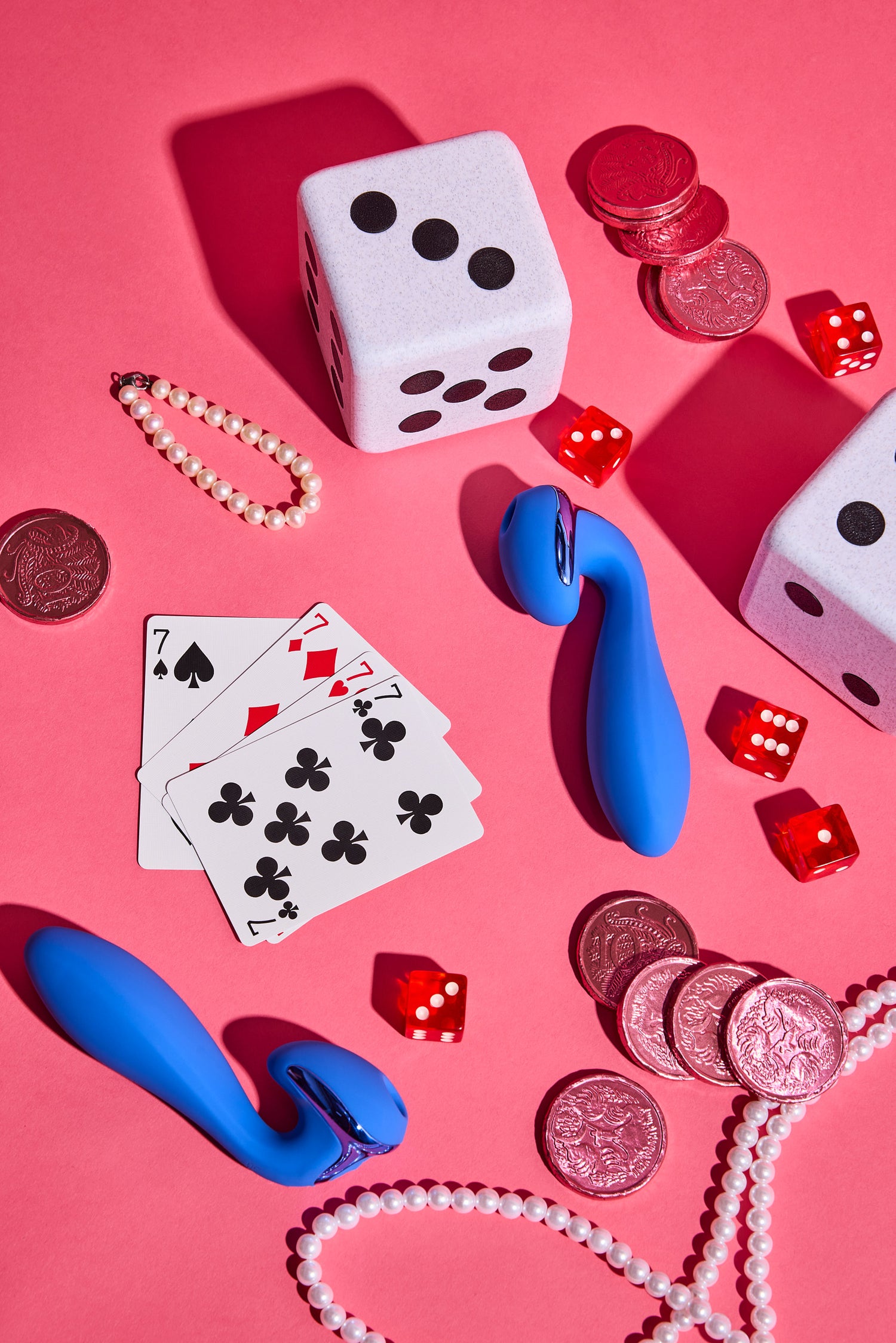 Blue toy, playing cards, dice, and coins on a pink background