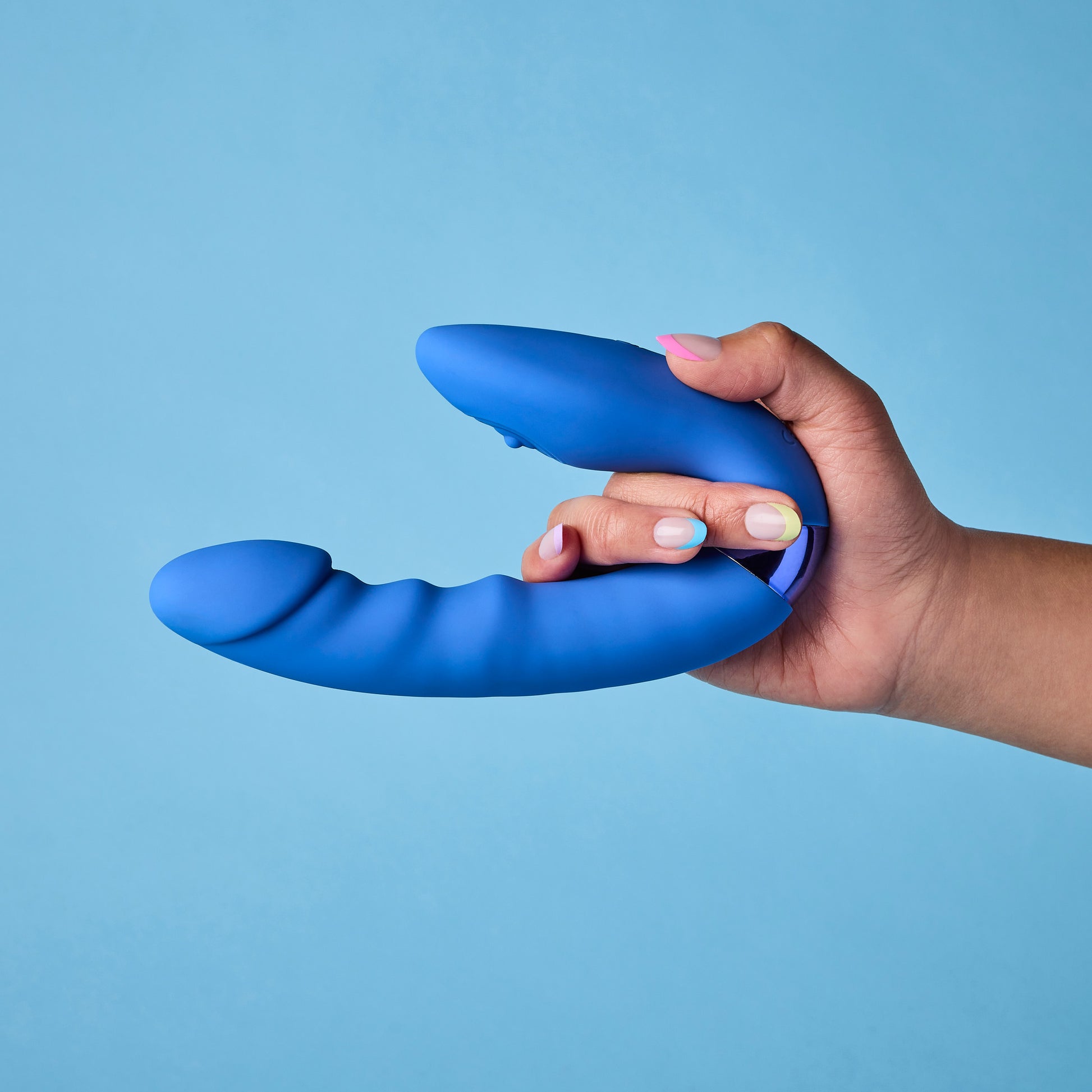 Hand holding a blue silicone vibrator against a light blue background